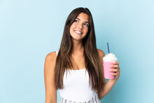 Young Brazilian Woman With Strawberry Milkshake Isolated On Blue Background Thinking An Idea While Looking Up