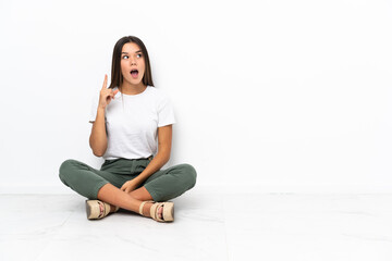 Wall Mural - Teenager girl sitting on the floor thinking an idea pointing the finger up