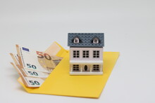 Banknotes In A Yellow Envelope And A Toy House, Funds For The Purchase Of Real Estate.