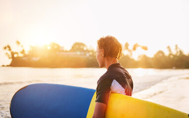 Wall Mural - Young teenager boy with colorful surfboard go to the sea for surfing. He enjoying a beautiful sunset light on Dewata beach on Sri Lanka. Active sport vacation and exotic countries traveling concept.