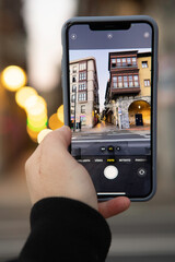 Hand of a person holding a phone taking a photo of a cityscape. Concept of telephone communication, social networks, mobile photography and travel.