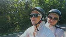 Two Caucasian Tourist Woman Man Drive On Red Scooter. Make It Selfie. Love Couple On Motorbike In White Clothes To Go On Forest Road Trail Trip.