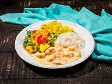 White Plate With Cream Prawns, Tomatoes, Carrots, Potatoes And Rice With Broccoli On Rustic Wood With Blue Liner,