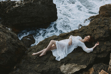 Poster - Beautiful bride Lies on his back on a stone cliff, cloudy weather vacation concept