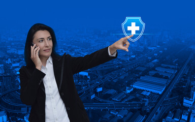 Wall Mural - Caucasian businesswoman talking on her cell phone and pointing finger to cross shape with shield icon over modern city tower, street, expressway and skyscraper, Business healthy and medical care insur