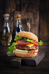 Wall Mural - Hamburger with bacon, turkey burger meat, cheese, tomato and lettuce on wooden background. Tasty burger. Close up