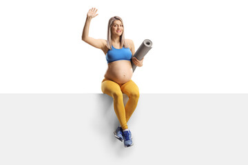 Wall Mural - Pregnant woman in sportswear with an exercise mat sitting on a blank panel and waving