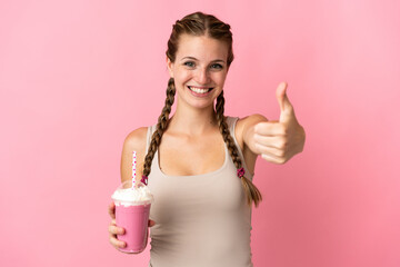 Wall Mural - Young woman with strawberry milkshake isolated on pink background with thumbs up because something good has happened