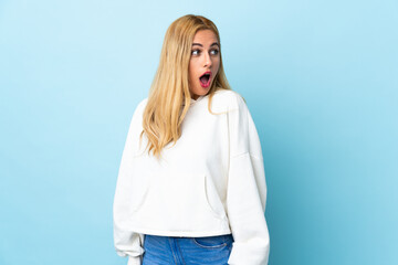 Wall Mural - Young Uruguayan blonde woman over isolated blue background doing surprise gesture while looking to the side