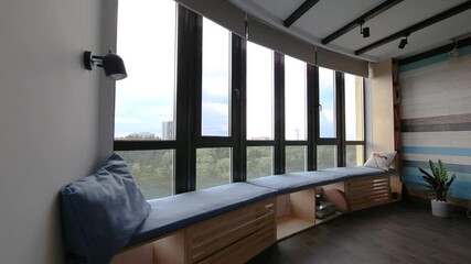 Poster - Video of motorized roller shades in the interior. Automatic roller blinds beige color close down on big glass windows. Remote Control Shades are above the windowsill with pillows. Summer. 
