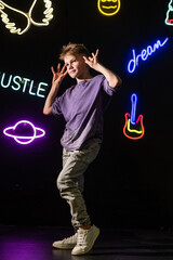 Stylish active guy in a purple T-shirt  having fun on neon signs background.