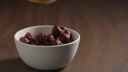 Wall Mural - Slow motion freeze-dried cranberries fall in white bowl on wood table with copy space