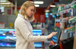 © M-Production - Woman pays at self-checkouts in supermarket.