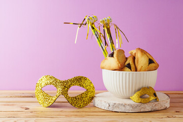 Wall Mural - Jewish holiday Purim concept with hamantaschen cookies  and carnival mask on wooden table over violet purple background.