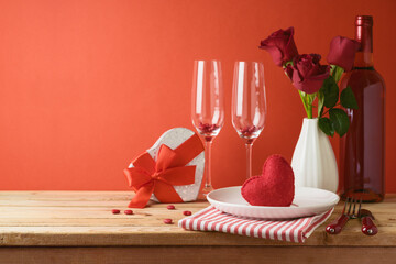 Wall Mural - Valentines day romantic dinner concept. Wooden table with plate, wine bottle and rose flowers over red background