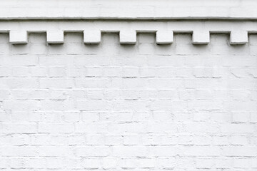 A white brick wall with decorative ornamental frieze on top