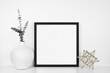 Mock up black square frame with modern home decor. White shelf against a white wall.  Eucalyptus branches in vase with geometric table top decoration. Copy space.
