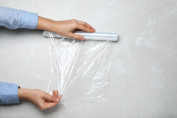 Wall Mural - Woman with roll of stretch wrap at light grey table, top view