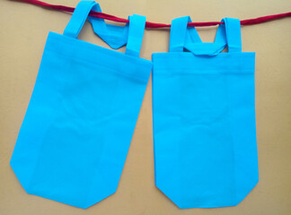 two light blue tote bags on a beige background hanging on a red string. bags made of polypropylene.