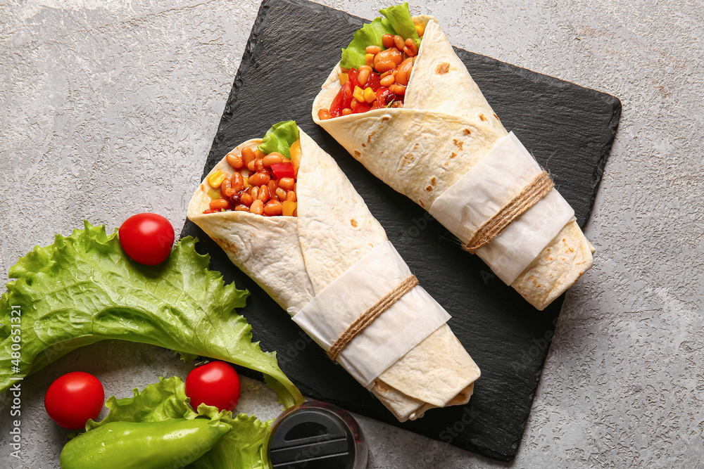 Slate plate with delicious burritos on grey background