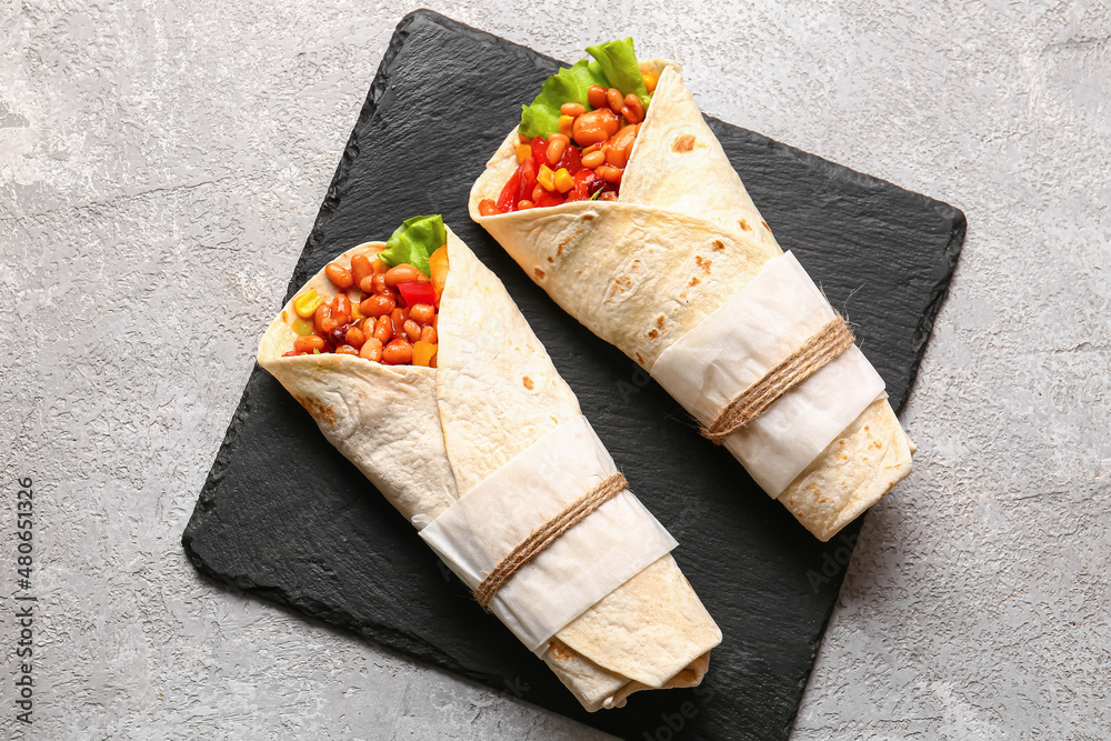 Slate plate with delicious burritos on grey background