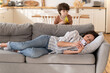 © DimaBerlin - Relaxed young woman mother or nanny ignore noisy little kid lying on sofa in living room with smartphone, browsing internet or mobile apps rest after work pay no attention to disturbing loud small son
