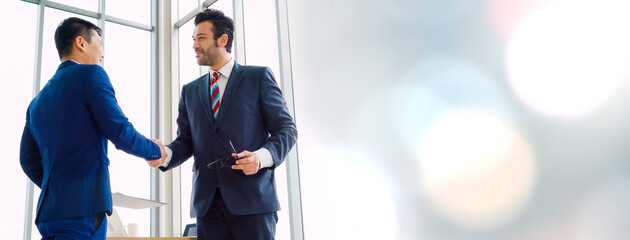 Business people handshake in corporate office in widen view showing professional agreement on a financial deal contract.