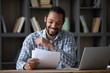 © fizkes - Happy cheerful African student guy reading admission letter from school, university, college, receiving paper document, smiling, laughing. Millennial businessman getting good deal, contract
