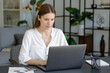 © kucherav - Young focused caucasian businesswoman sitting at desk working on a laptop computer in contemporary office