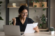 Sincere cheerful young hispanic latin woman in eyewear reading paper document, reading amazing win news, celebrating success, feeling overjoyed getting new business opportunities at home office,