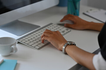 Poster - Cropped image of woman hand typing on a wireless keyboard and using wireless mouse at the white modern working desk.
