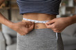 Close up millennial gen sporty fit woman measuring waist line with tape after active workout at home, feeling satisfied with burn out weight loss exercises results, healthy dietary lifestyle concept.