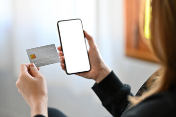 Poster - Cropped image of a businesswoman holding a white blank screen mobile and credit card in the modern living room.