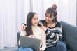 © Thirawatana - Lgbtqia. Two women use laptop computer on the sofa in the living room.