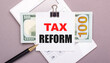 © Елена Дигилевич - On a gray background, a white calculator, a pen, banknotes and a sheet of paper under a black paper clip with the text TAX REFORM. Business concept