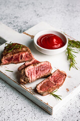 Wall Mural - Juicy slices of Rib Eye beef steak on a wooden board with rosemary and tomato sauce