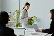 Portrait of young Asian businesswoman speaking to colleagues while sitting on table during business meeting, copy space
