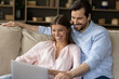 © fizkes - Young 30s couple relaxing at home sit on couch in living room using laptop, make order, discuss purchase, enjoy comfort e-services through retail ecommerce services. Modern tech, e-shopping concept
