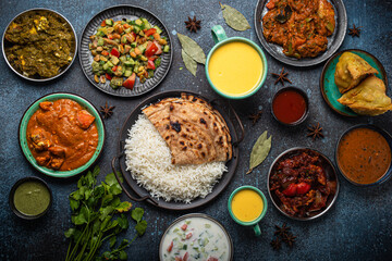 Wall Mural - Assorted Indian ethnic food buffet on rustic concrete table from above: curry, fried samosa, rice biryani, dal, paneer, chapatti, naan, chicken tikka masala, mango lassi, dishes of India for dinner