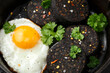 Cooked Black Pudding with egg, herbs and parsley on iron cast pan