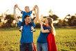 Mother, father and son in superhero costumes. Parents hold their son in their arms and play superhero outdoors