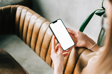 Woman holding mobile phone with white screen mock up, resting on a sofa in living room at home.	