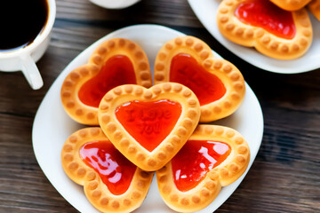 Heart shaped red jam cookies and two cups of coffee on a brown wooden background.