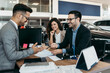 © Dusko - Middle age couple choosing and buying car at car showroom. Car salesman helps them to make right decision. Man signs buyers contract.