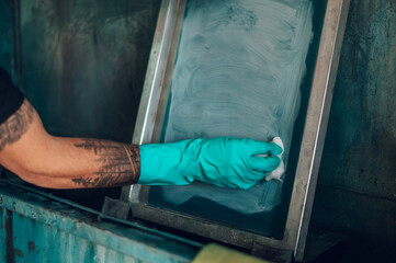 Wall Mural - Male worker cleaning screen frame with a cloth in a printing workshop