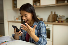 Happy Excited Woman Shouting Looking At Screen Of Her Mobile Phone , After Learning Unbelievable Prefect News Or Receiving Invitation To Long-awaited Party, Isolated On Kitchen Background