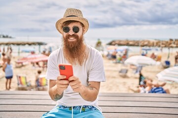 Sticker - Young redhead tourist man using smartphone sitting on the bench at the beach.