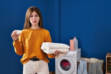 Canvas Print - Young brunette woman holding detergent and clean laundry skeptic and nervous, frowning upset because of problem. negative person.