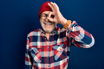 Poster - Handsome mature man wearing hipster look with wool cap doing ok gesture with hand smiling, eye looking through fingers with happy face.