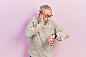 Wall Mural - Handsome senior man with beard wearing casual sweater and glasses looking at the watch time worried, afraid of getting late